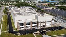 A large, modern industrial building with “Cologix” signage, surrounded by parking lots, roads, and green lawns in a suburban business area.