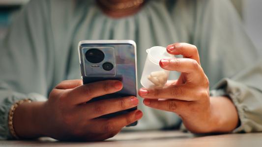 A person holding a smartphone in one hand and a small container with pills in the other, possibly using ChatGPT to seek healthcare advice or medication information.