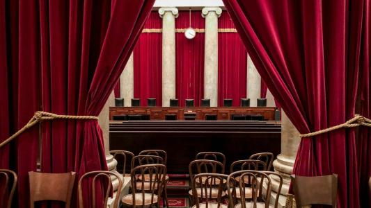 View of a courtroom through parted red curtains, revealing wooden chairs and a judge's bench flanked by large pillars, reminiscent of the grandeur often seen in images of the Supreme Court shared on social media.