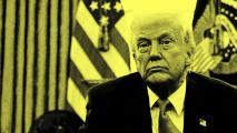 A man in a suit sits in a room with American flags behind him. The image is in high contrast with a yellow tint.